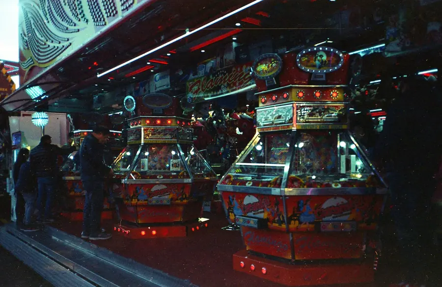 Red and gold amusement cabinets glowing under strings of lights in a night-time arcade with a few visitors