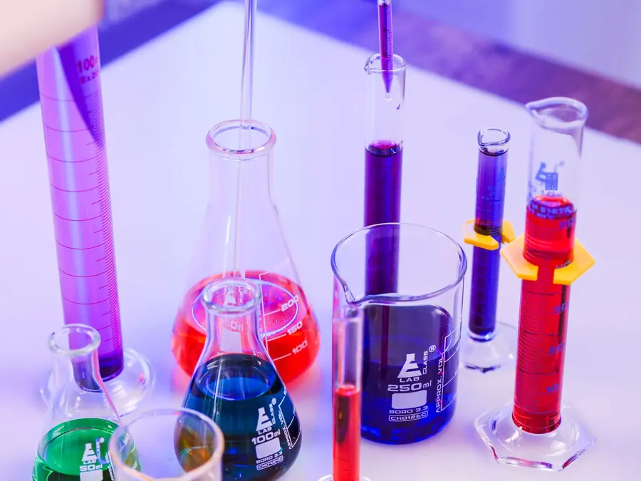 Lab flasks, beakers and cylinders filled with bright pink, red, blue and green liquid on a white bench