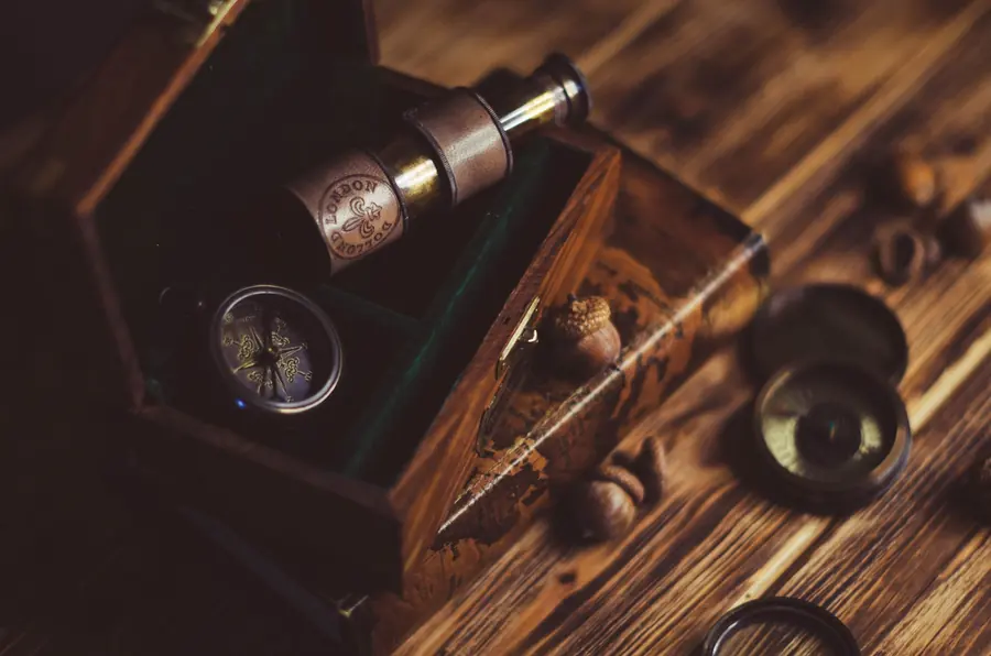 A brass compass and a small telescope resting in a green-lined wooden box on a rough plank table